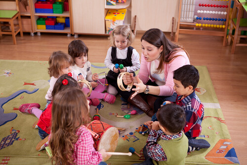 Une animatrice et de jeunes enfants jouant de la musique en cercle dans une classe de maternelle.